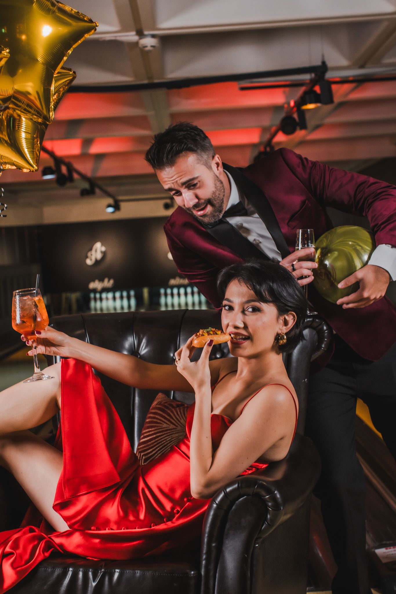 A man and woman in matching red dresses sit together on a cosy couch, enjoying each other's company.
