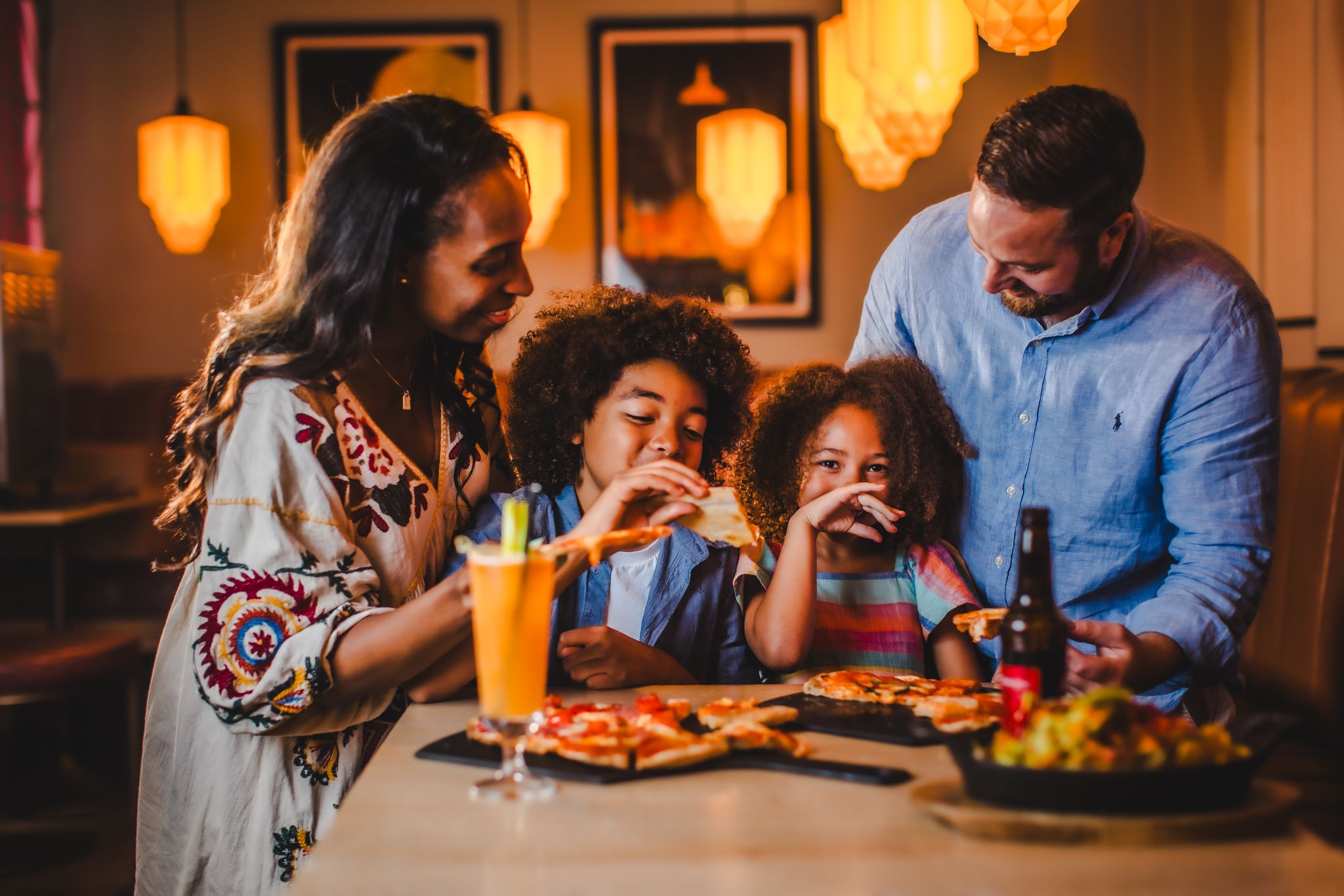 A family smiling whilst eating food at a table.